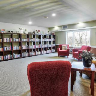 A cozy library with red chairs and bookshelves filled with books, offering a bright reading area by the window.