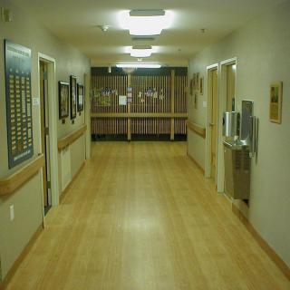 A quiet hospital hallway with wooden flooring and fluorescent lighting.
