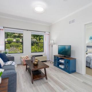 A modern living room with a sofa, television, and large windows overlooking greenery.