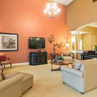 A cozy living room with elegant furnishings, featuring a large sofa, a television on an accent wall, and a chandelier overhead.