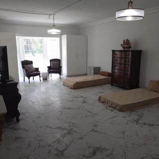 A minimalist living room with floor mattresses, two chairs by a window, and a tall dresser.
