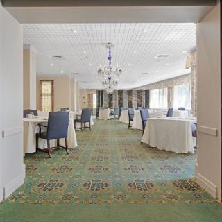 A spacious conference room with round tables and comfortable chairs, illuminated by a large chandelier and natural light.