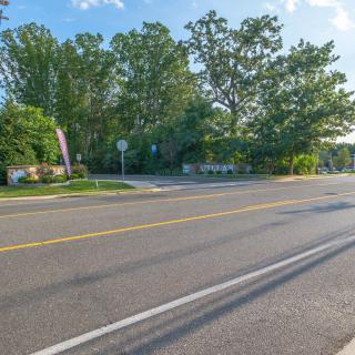 A quiet road intersection surrounded by lush green trees under a clear blue sky.