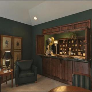 A cozy home bar with classic wooden cabinetry and dark green walls, featuring a seating area with armchairs.