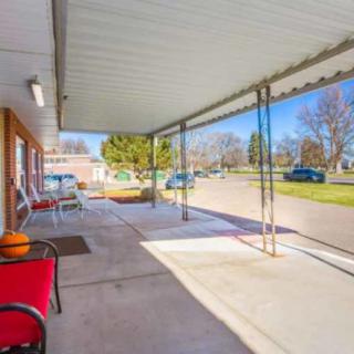 A suburban patio with outdoor seating, covered by an awning, overlooking a driveway on a sunny day.