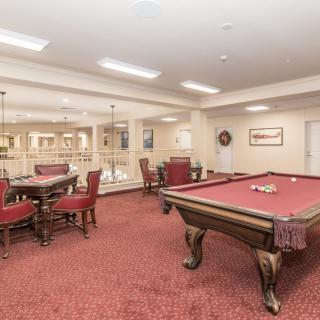 A spacious game room featuring a pool table and seating area with red carpet flooring.