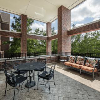 A spacious outdoor patio with a table, chairs, and a sofa surrounded by brick pillars and greenery.