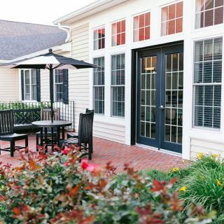 A cozy patio area featuring outdoor seating with an umbrella, surrounded by a garden with vibrant flowers.