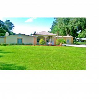 A single-story house with a spacious green lawn and surrounding trees, showcasing a peaceful residential setting.
