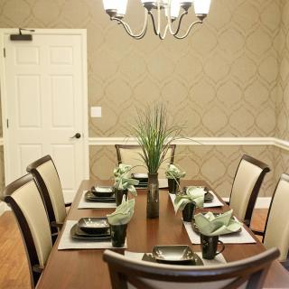 A well-decorated dining room with a wooden table set for six, featuring elegant place settings and central plant decorations under a chandelier.