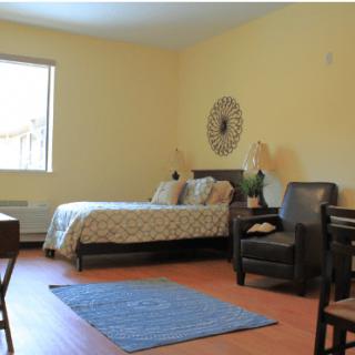 A cozy bedroom featuring a bed, armchair, and window, with stylish decor on the wall.