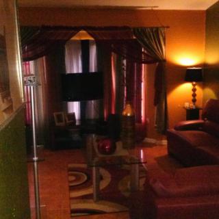 A warmly lit living room featuring a sofa, television, and elegant curtains.