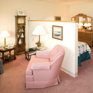 A cozy living space with a pink armchair, lamps, and a partially visible bedroom in the background.