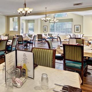 A spacious dining room in a restaurant with neatly arranged tables and chairs, elegant chandeliers, and large windows.