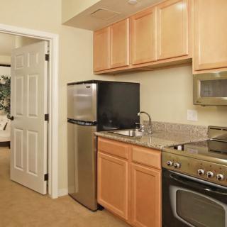 A compact apartment kitchen with light wood cabinets, stainless steel appliances, and a granite countertop.