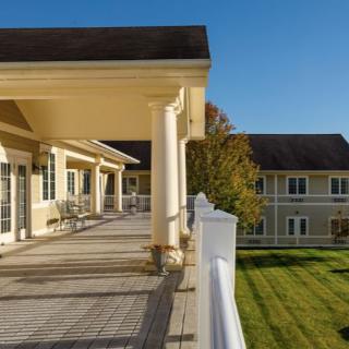 A sunny day view of a building with a spacious porch and well-maintained lawn.