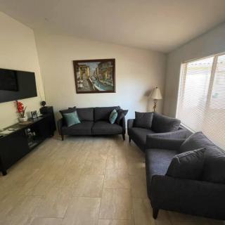 A well-lit living room featuring dark sofas, a wall-mounted television, and a decorative painting.