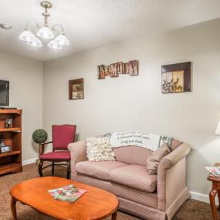 A cozy living room with a sofa, armchair, and coffee table, decorated with wall art and a bookshelf.