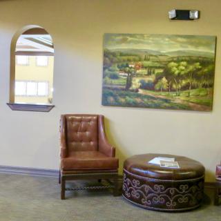 A cozy seating area with a leather chair, decorative round table, and landscape painting on the wall.