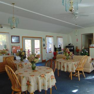 A cozy dining area with round tables and chairs, featuring decorative lighting and flowers on the tables.