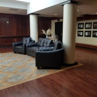 A cozy lobby area featuring black leather sofas and a warm wooden floor, accented by decorative columns and framed photographs on the wall.