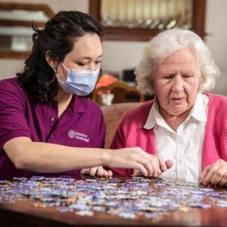 A caregiver helps an elderly woman with a puzzle at home.