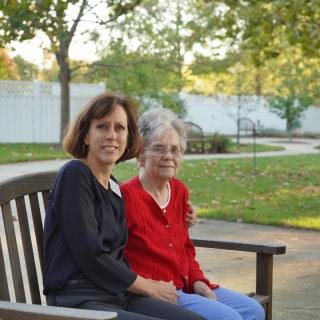 Two women sitting on a bench in a park during the day.