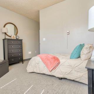 A cozy bedroom with a neatly made bed, featuring colorful pillows and a blanket, alongside a dresser with a round mirror on the wall.