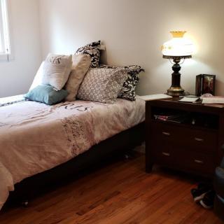 A cozy bedroom with a neatly made bed, featuring multiple pillows and a nightstand with a lamp.