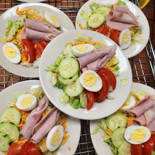 A colorful assortment of fresh salads served on individual plates, featuring vegetables and sliced ham.