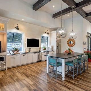 A modern kitchen featuring an open design with a central island, wooden flooring, and stylish pendant lights.