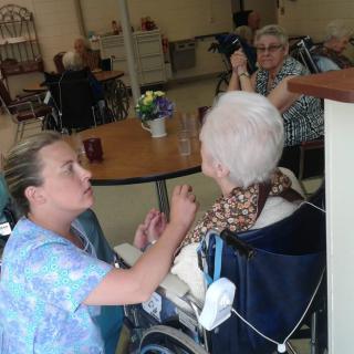 A healthcare worker assists an elderly person in a nursing home setting.