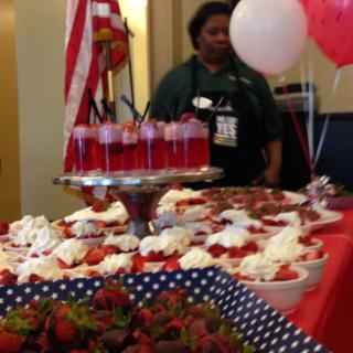 A festive dessert table adorned with various strawberry dishes and decorations, including balloons and a flag.