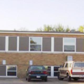 A two-story brick building with parked cars in front, taken during the daytime.