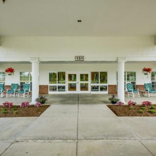 A building entrance with columns, landscaping, and chairs outside.