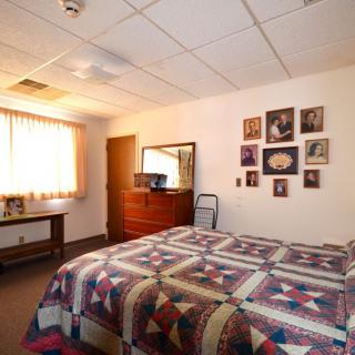 A cozy bedroom with a quilted bedspread and family photos decorating the wall.