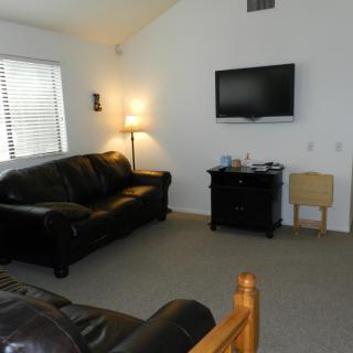 A cozy living room with a sofa, wall-mounted television, and a lit floor lamp.