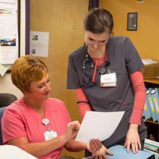 Two nurses in scrubs discussing a document in a healthcare setting.