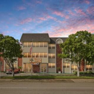 A multi-story building sits along a road, framed by trees under a colorful dusk sky.