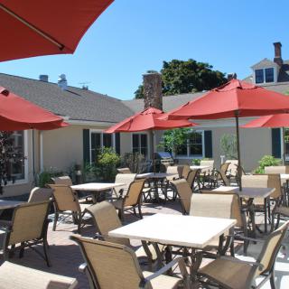 A sunny outdoor patio with tables and chairs, shaded by red umbrellas.