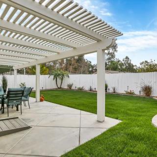 A well-maintained backyard with a covered patio and outdoor seating, featuring a lush green lawn and surrounding fence.