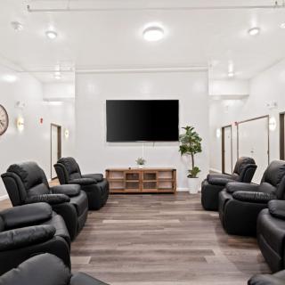 A modern living room with black recliners arranged around a large television on a wooden floor.