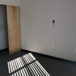 An empty room with sunlight casting shadows through a window, featuring a sliding door and minimalist decor.