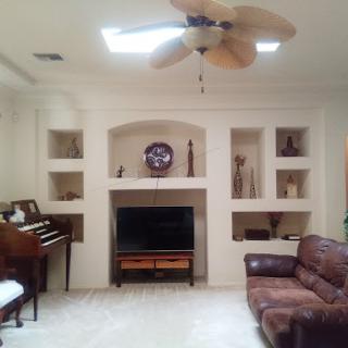 A cozy living room featuring a piano, a TV setup, and decorative shelves.