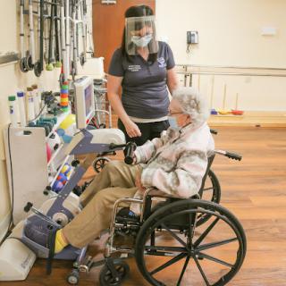 A healthcare worker assists an elderly patient in a wheelchair with medical equipment.