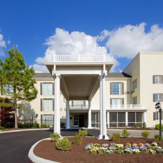 A modern hotel with a grand entrance and well-maintained landscaping under a bright, cloudy sky.