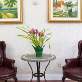 A cozy living room setup with two leather chairs, a round table adorned with a flower vase, and framed paintings on the wall.