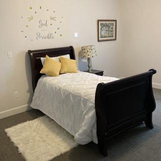 A cozy bedroom featuring a dark wood sleigh bed with white bedding and yellow accent pillows, accompanied by a nightstand and decorative lamp.