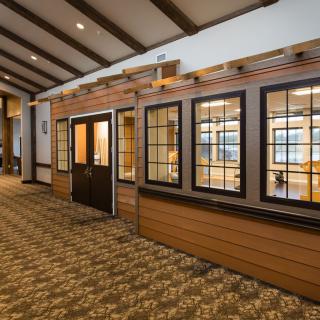 A hallway featuring wooden window panels and a carpeted floor with ceiling beams and soft lighting.