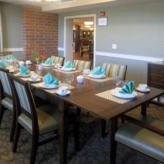 A neatly set dining table with blue napkins and chairs in a well-lit room.